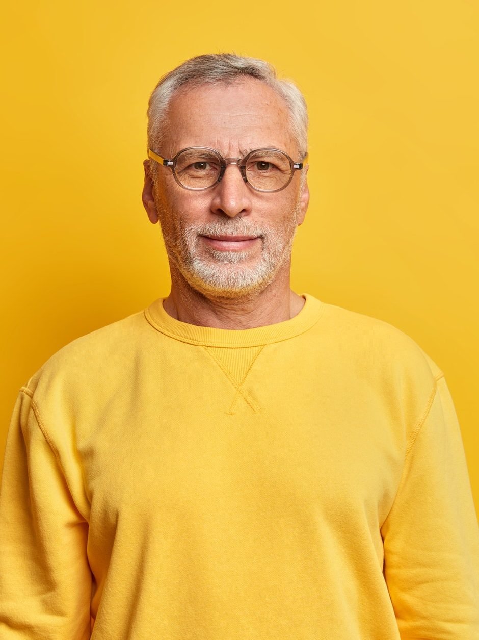 horizontal shot of grey haired man with wrinkles wears glasses and casual yellow jumper looks direct e1619343971741.jpg