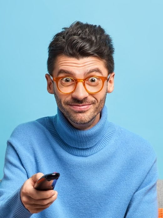 pleased unshaven man changes tv channels with remote control watches funny program dressed in casual e1619344021616.jpg