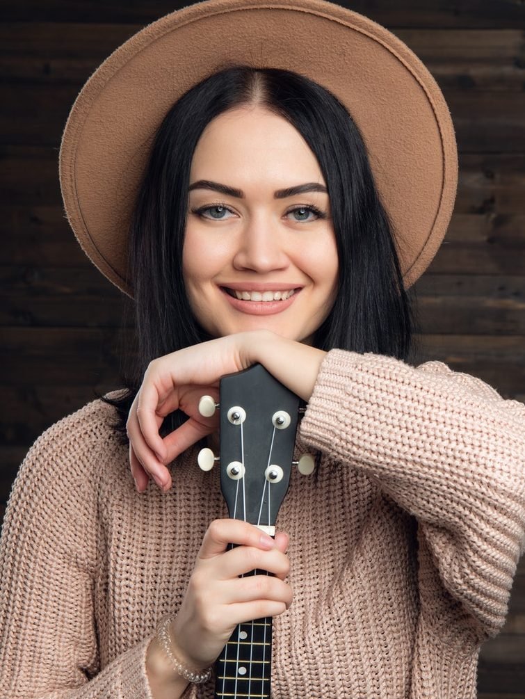portrait of a smiling casual woman posing with guitar against wooden plank e1619344484480.jpg